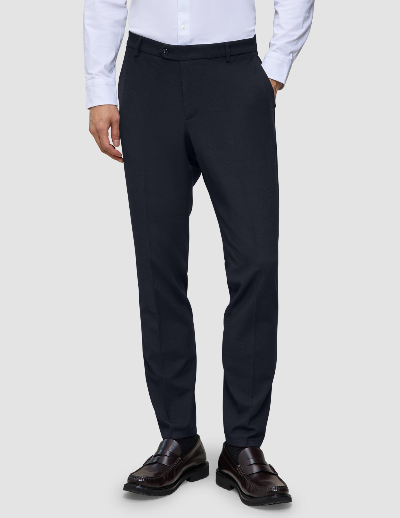 Motion Suit Pants Slim – Midnattsblå dressbukser i slim fit, kombinert med en hvit skjorte med knapper og brune loafers.